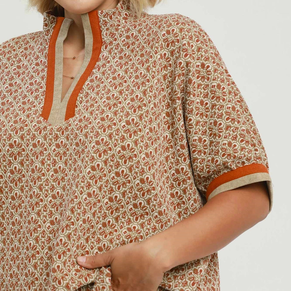 Close-up of a chestnut geometric print top featuring a split neckline and rust-orange contrast trim.