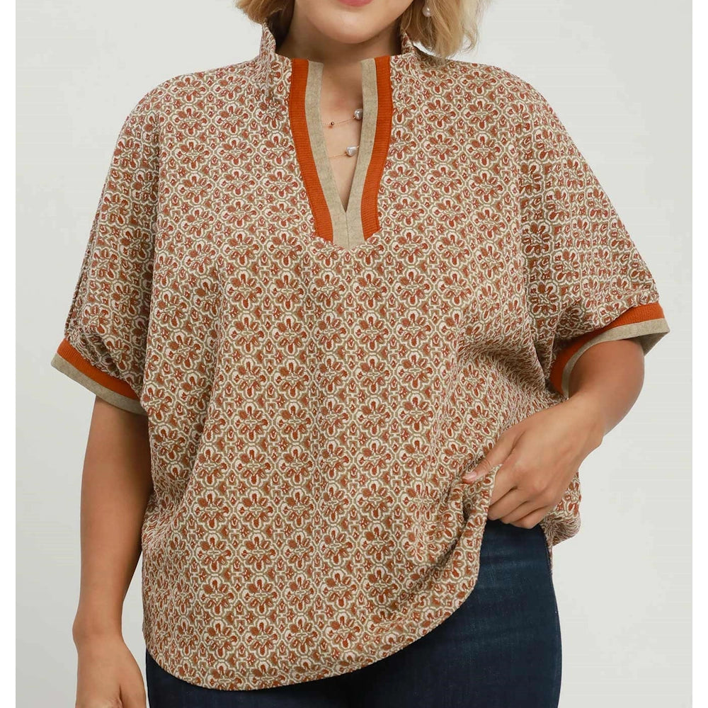 Woman wearing a chestnut geo print split-neck blouse with short sleeves paired with dark blue jeans.