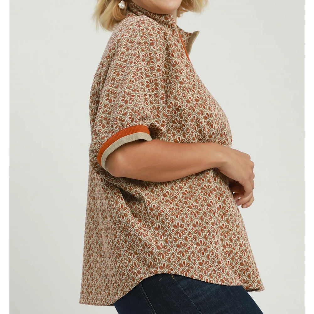 Side view of woman wearing chestnut geo print short-sleeve blouse with folded cuffs and split neck.
