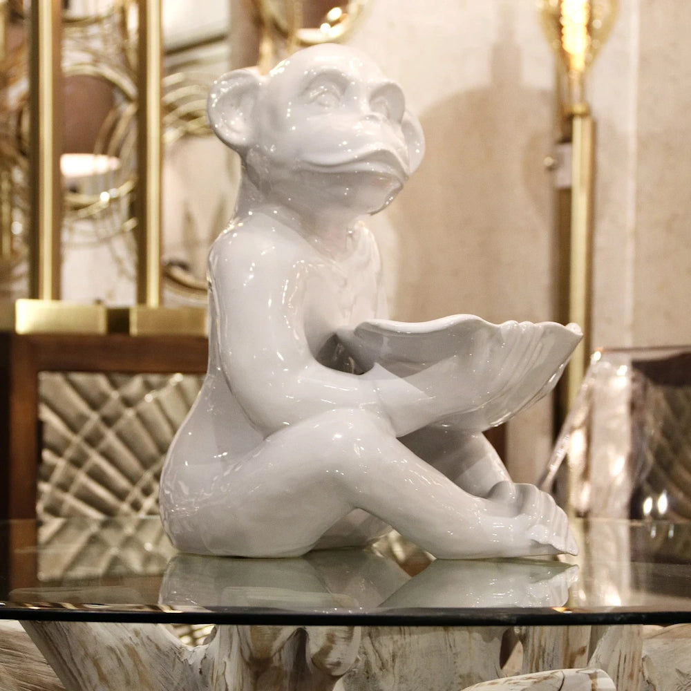 White ceramic monkey figurine holding a shell-shaped bowl on a glass table, elegant home decor accent.