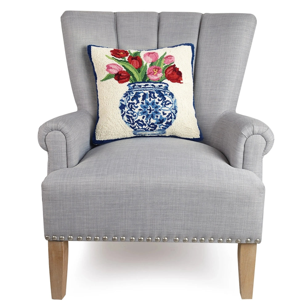 Chinoiserie tulip hook pillow on a grey wingback armchair with nailhead trim on a white background.