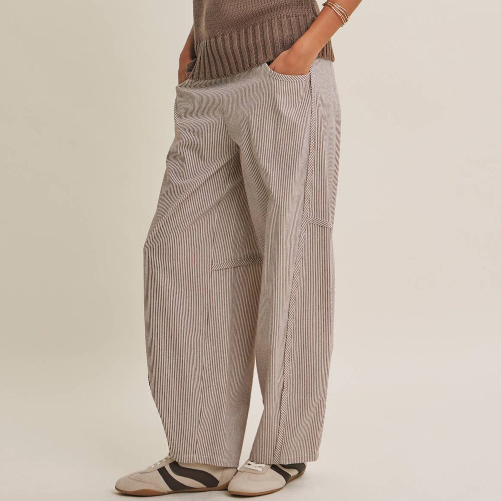 Person wearing relaxed brown vertical-striped barrel-leg pants with hands in pockets and casual sneakers.