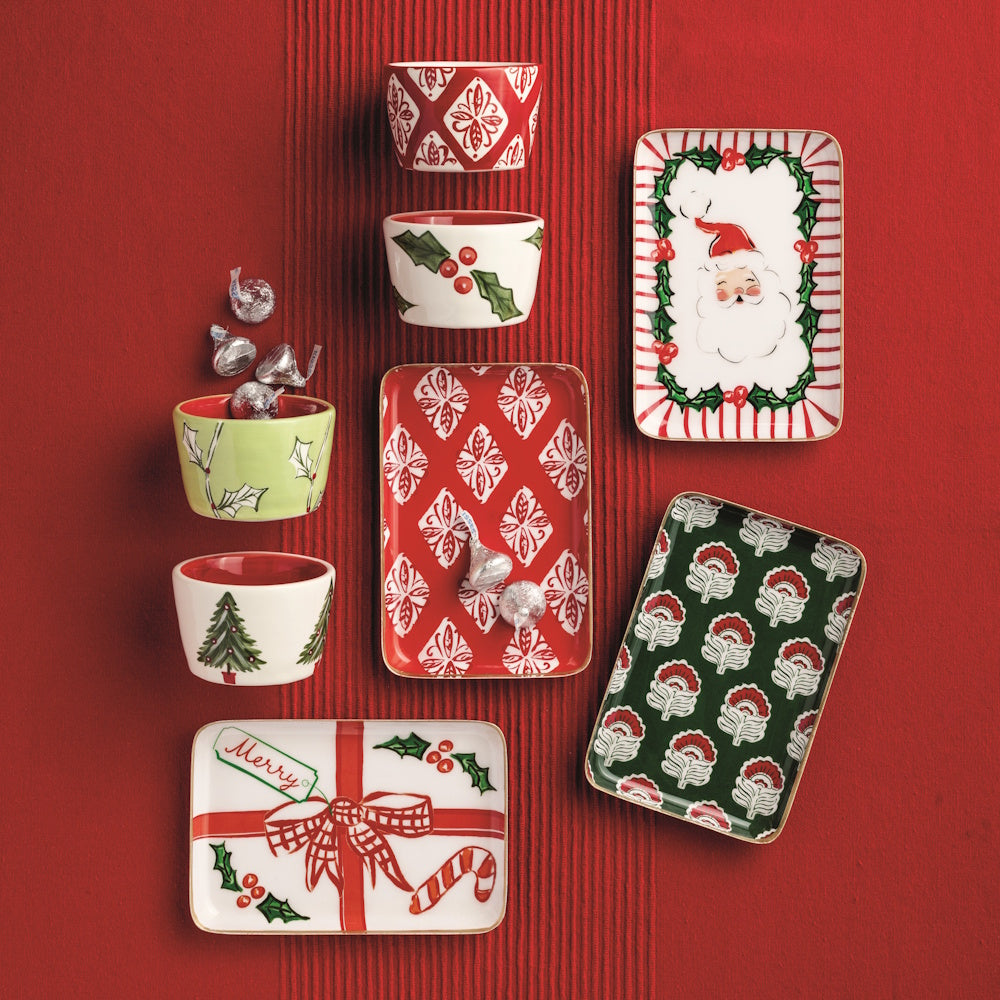 Lifestyle shot of the Christmas metal tidbit plates and matching bowls styled on a red fabric background.