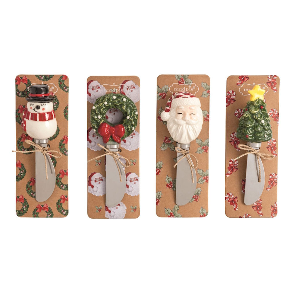 Four holiday cheese spreaders with ceramic handles shaped as a snowman, wreath, Santa, and Christmas tree.
