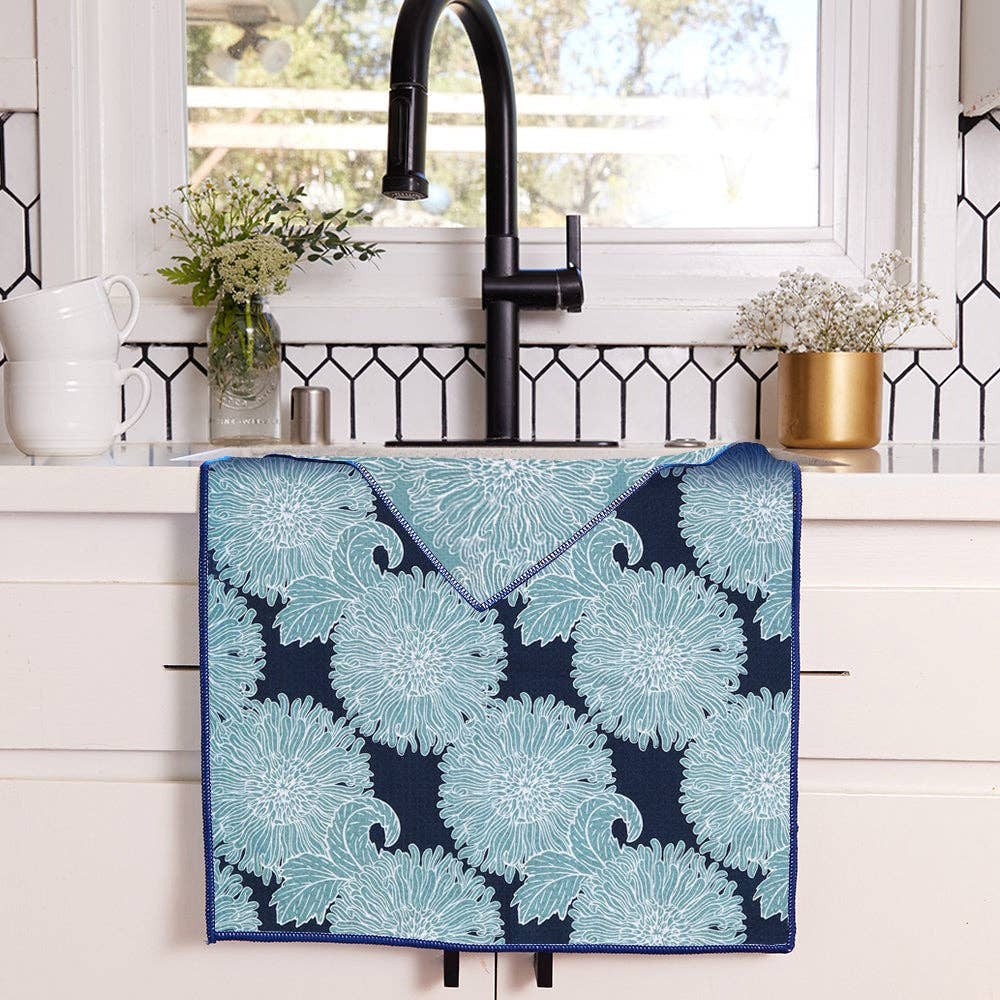 Blue chrysanthemum pattern eco-friendly kitchen tea towel draped over a white farmhouse sink with a black faucet.