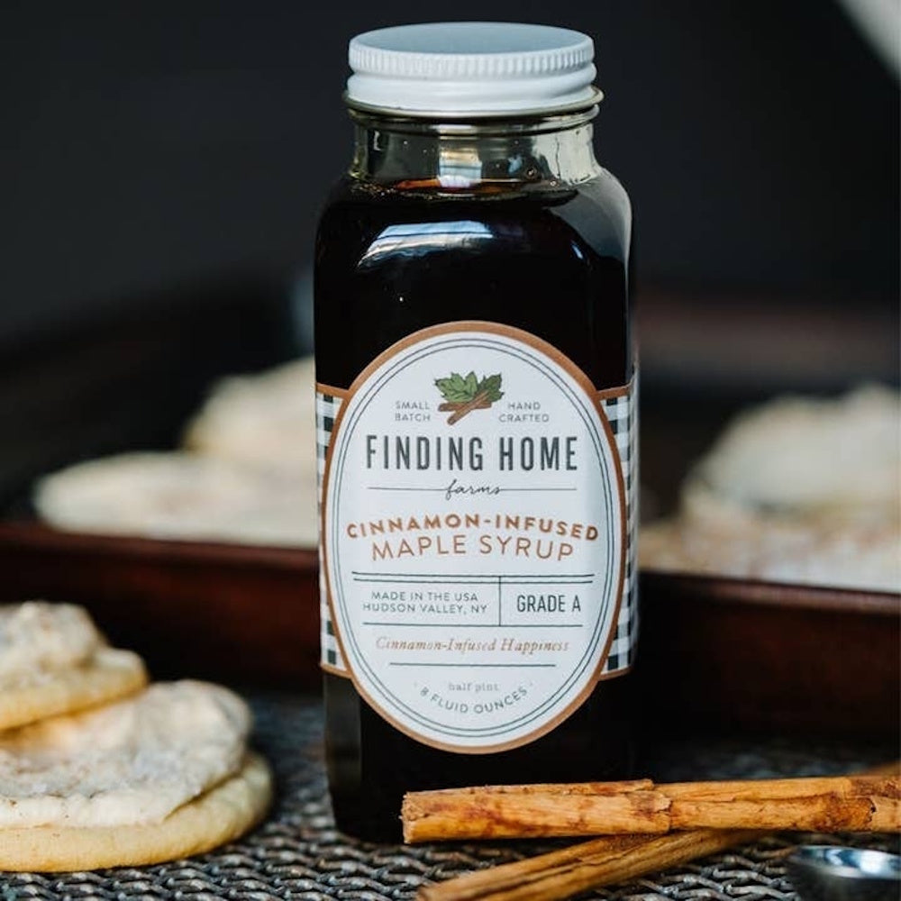 Glass bottle of Finding Home Farms cinnamon-infused maple syrup next to cinnamon sticks and pastries.