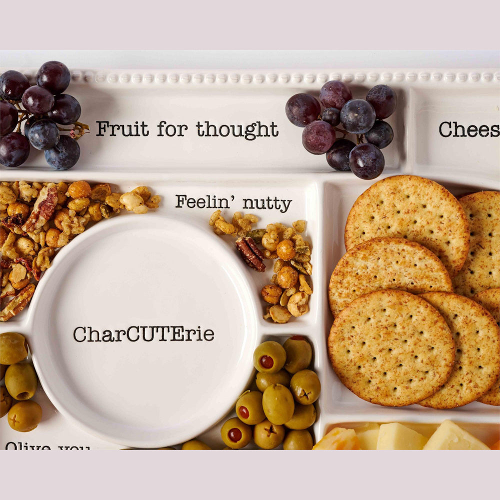 White ceramic charcuterie tray with sections for grapes, nuts, olives, and crackers, featuring playful stamped typography.