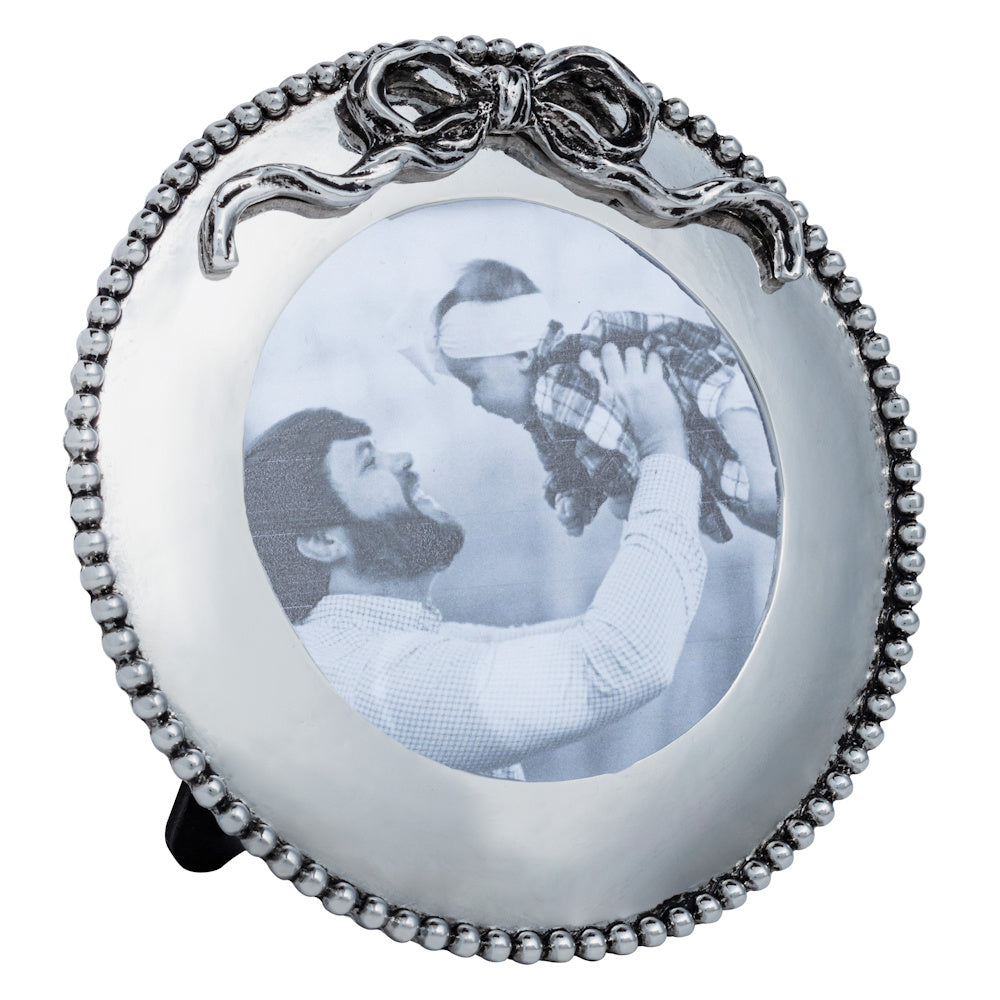 Small round silver picture frame with beaded edge and bow detail, holding a black and white photo of a father and child.