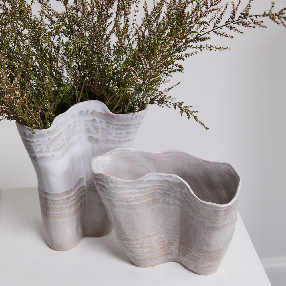 Two wavy, organic-shaped ceramic vases with white and beige textured glazes, one holding green branches.