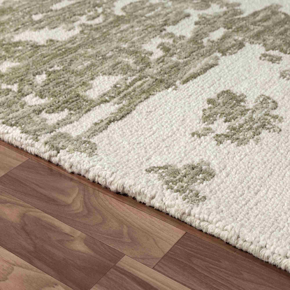 Close-up of a hand-tufted Nuvia rug with a green and ivory textured pattern on a dark wood floor.