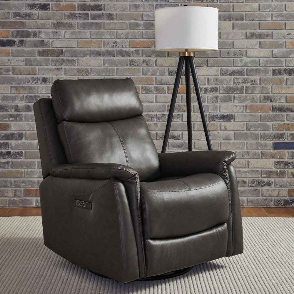 A dark gray leather recliner armchair next to a tripod floor lamp in front of a brick wall.