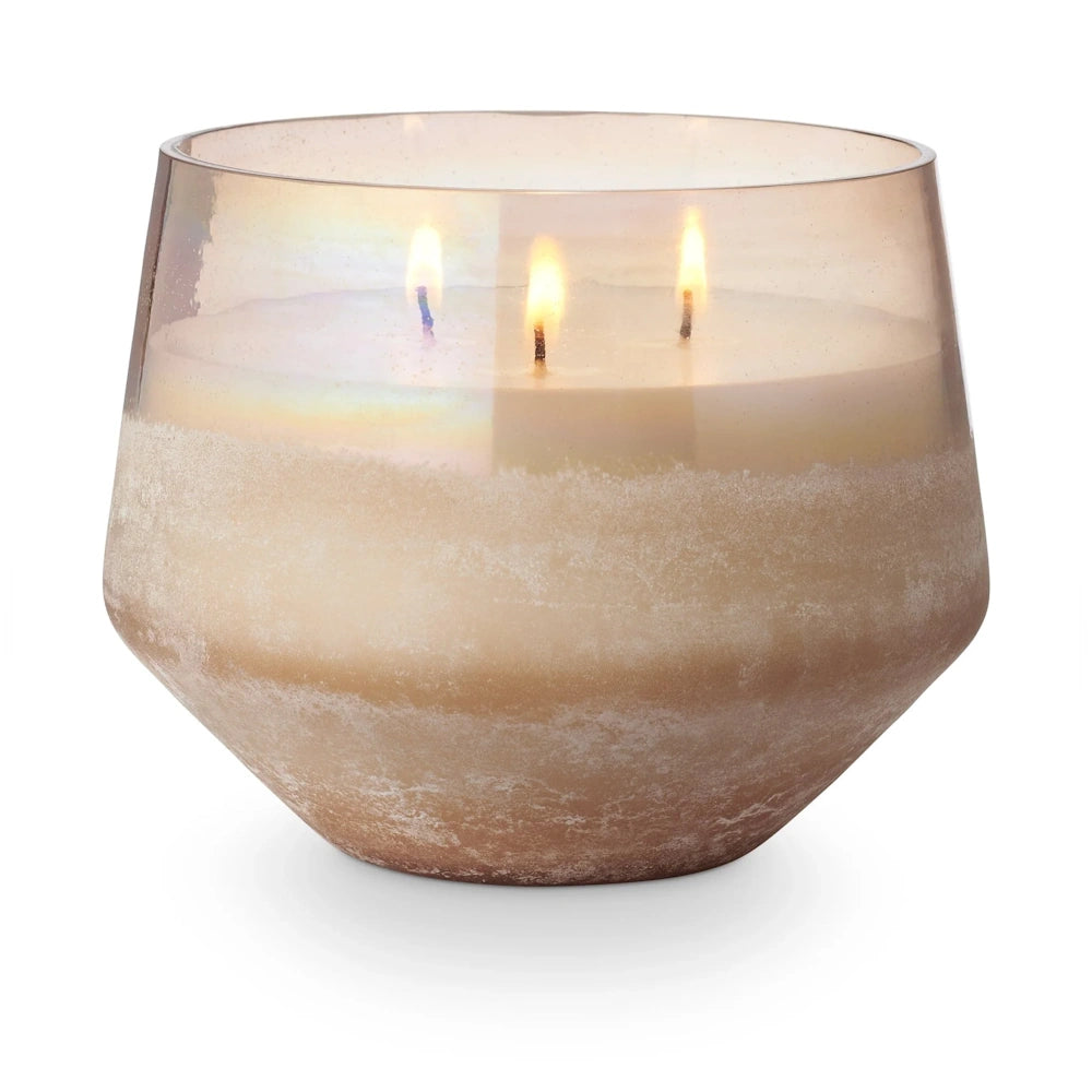 Three-wick coconut milk mango scented candle in a large iridescent baltic glass jar with a warm glowing flame.