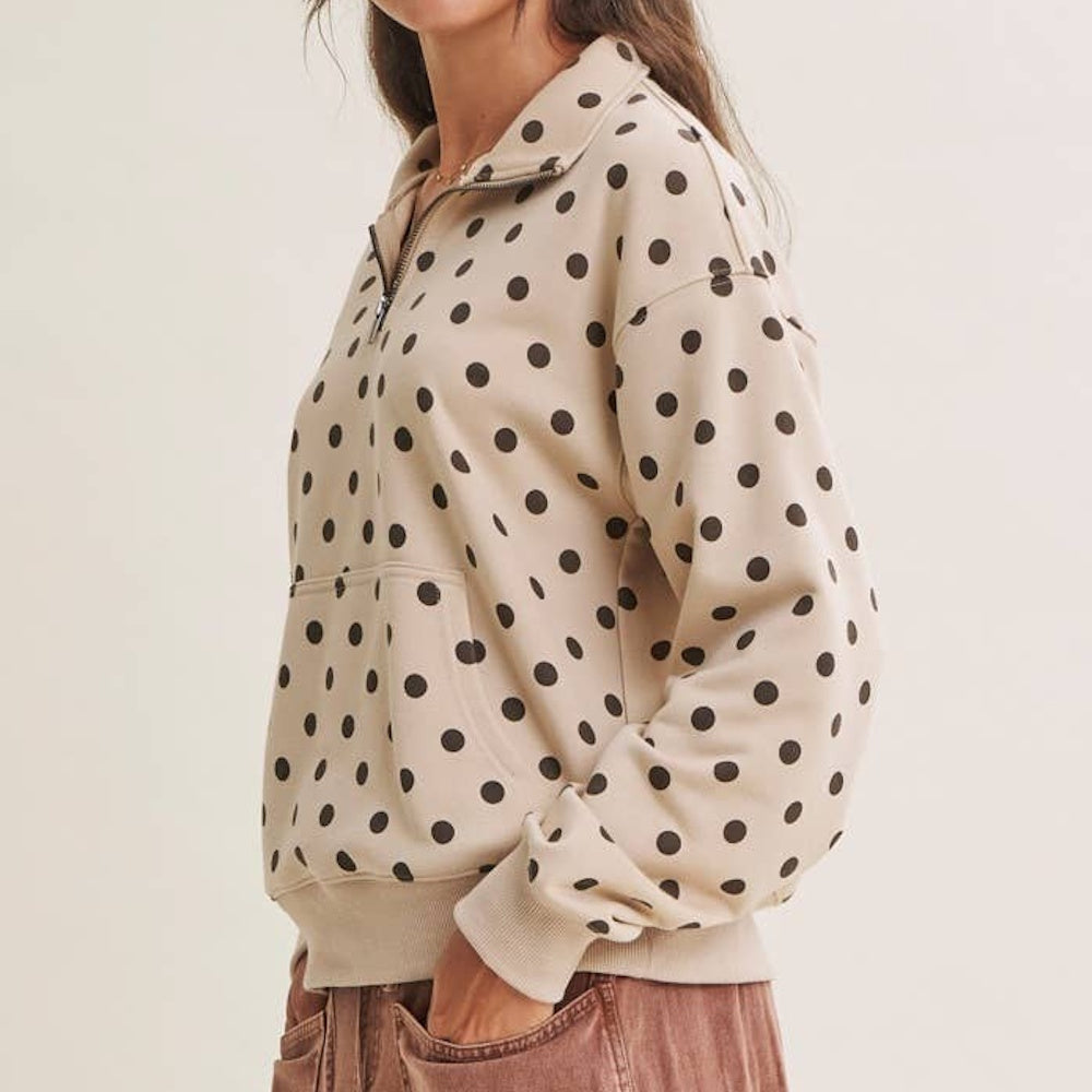 A person wearing a beige half-zip pullover with a brown polka dot pattern from a side view.