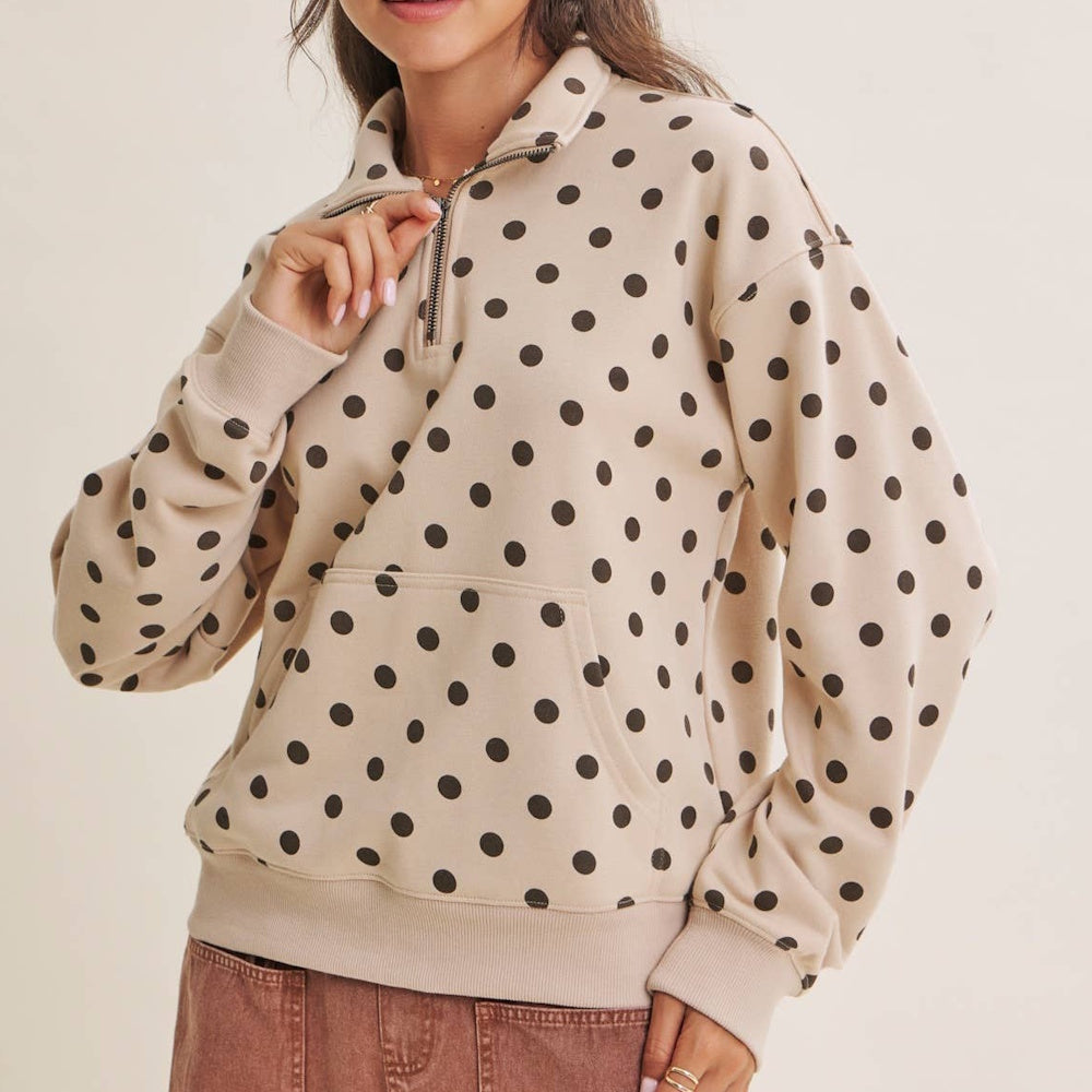 A person wearing a beige half-zip pullover with a brown polka dot pattern and a front pocket.