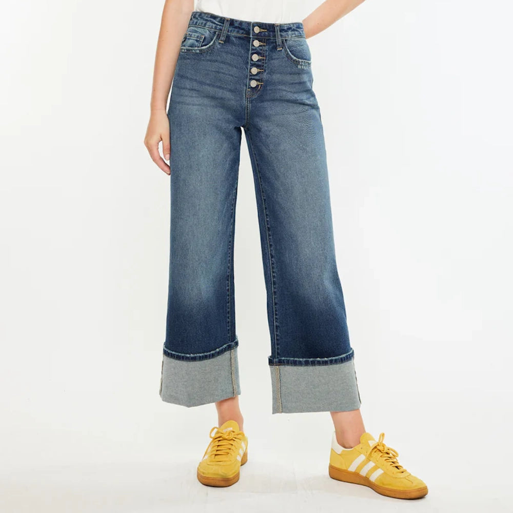 High-rise wide-leg crop jeans in dark wash with button fly and large cuffed hems, paired with yellow sneakers.