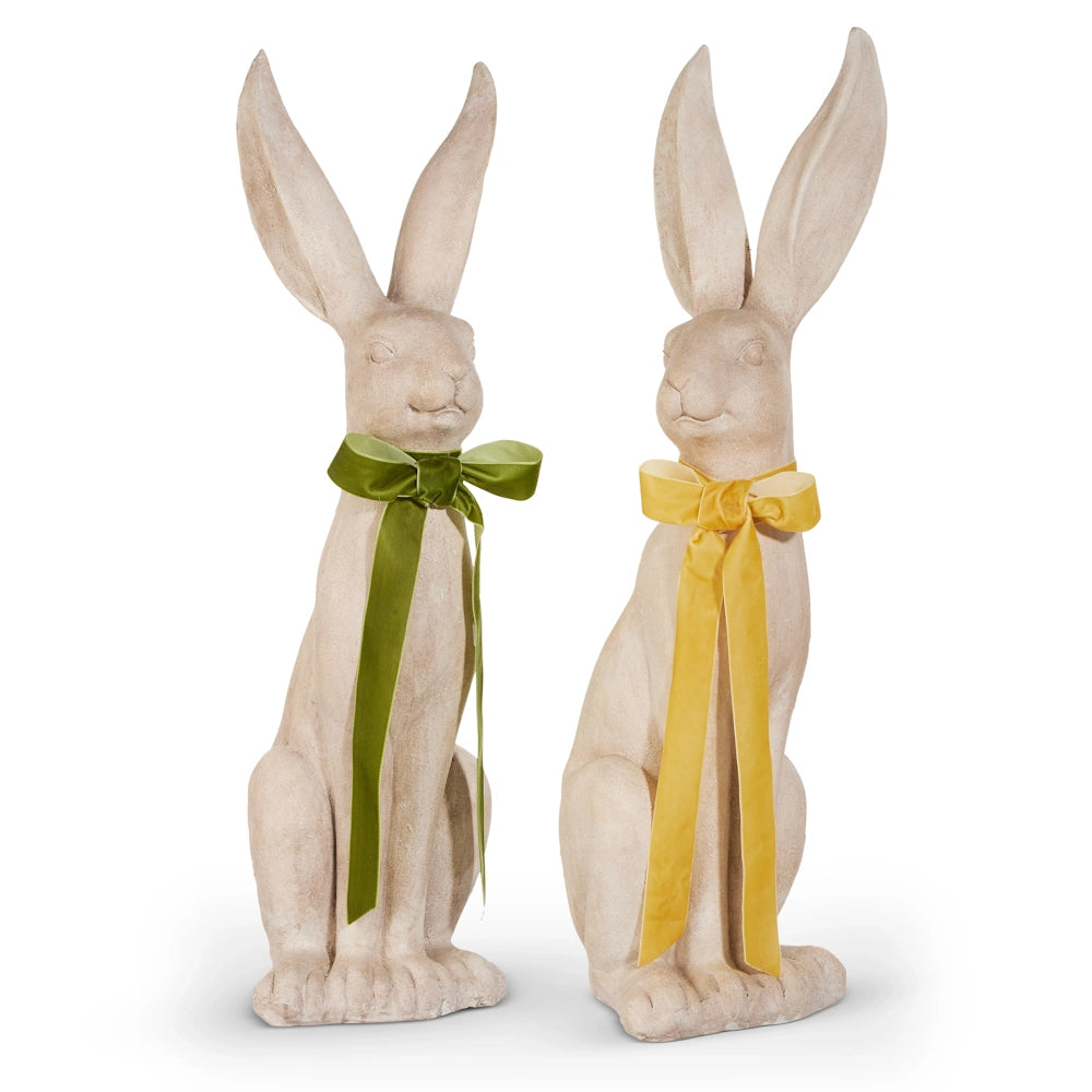 Two stone rabbit statues with large ears, one with a green bow and the other with a yellow bow. Their expressions convey a sense of calm and elegance.