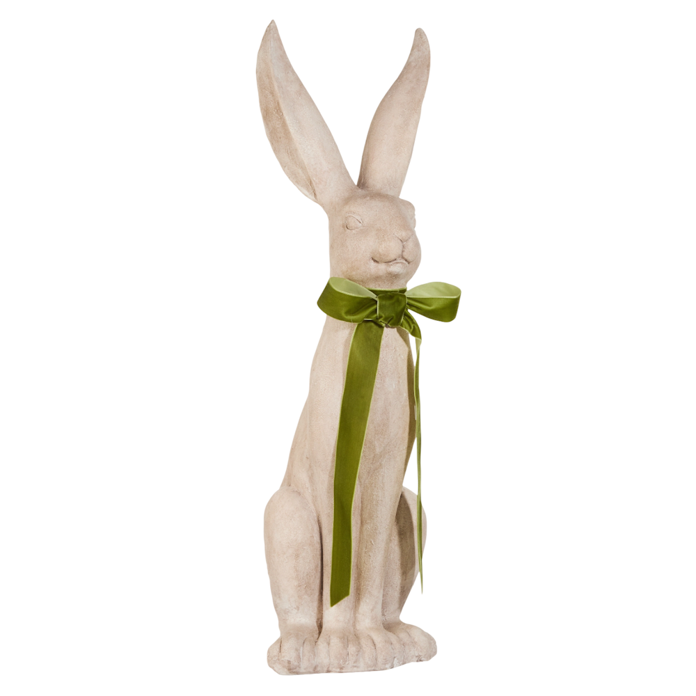 A tall, stone-colored rabbit sculpture with long ears sits upright, wearing a big green bow. The expression is serene, conveying elegance and whimsy.