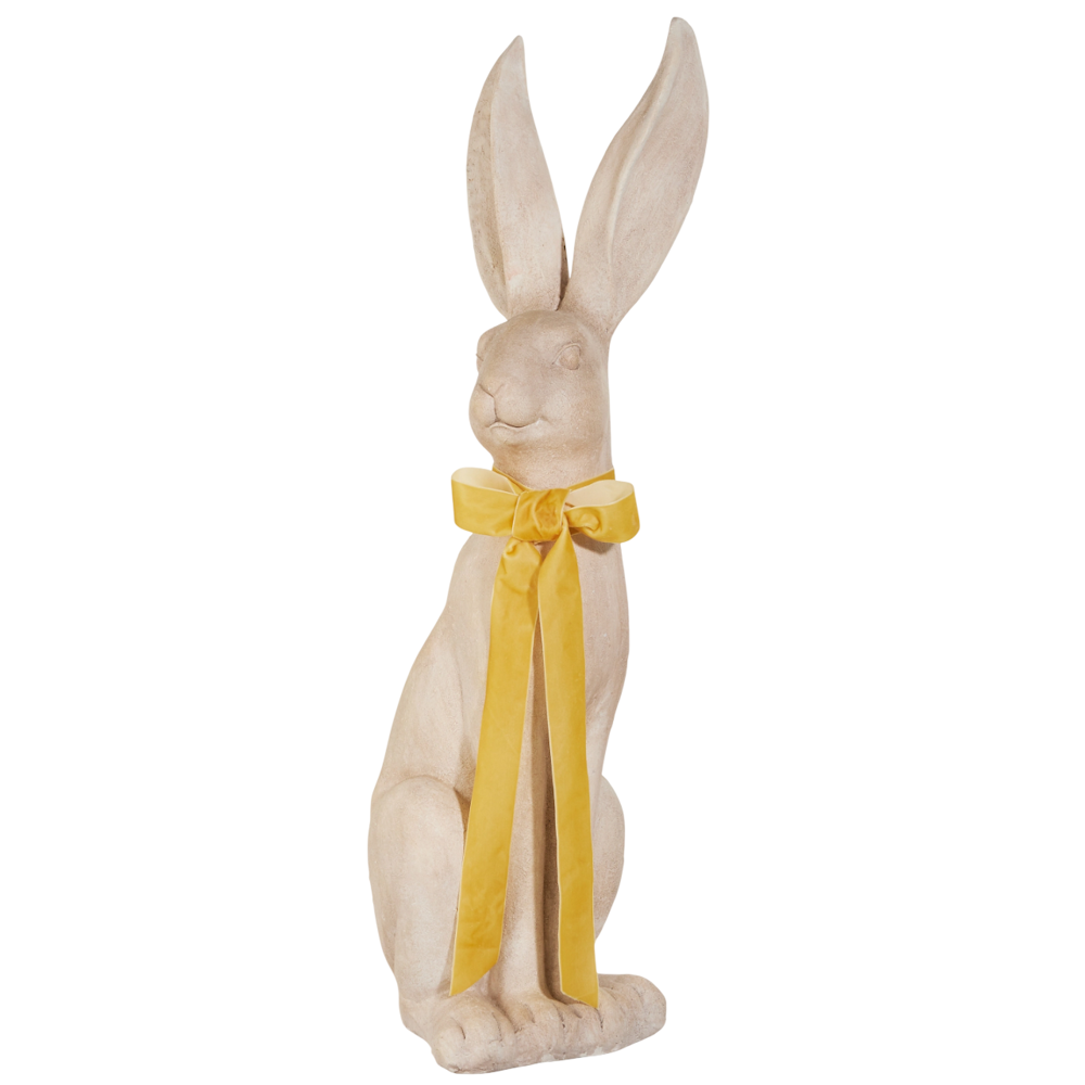 Statue of a beige rabbit with large ears, seated upright. It has a vibrant yellow bow tied around its neck, conveying a whimsical and elegant feel.
