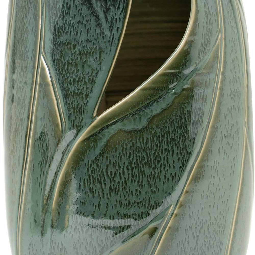 Close-up of a green ceramic vase featuring an open, cutout leaf pattern and a textured glaze.