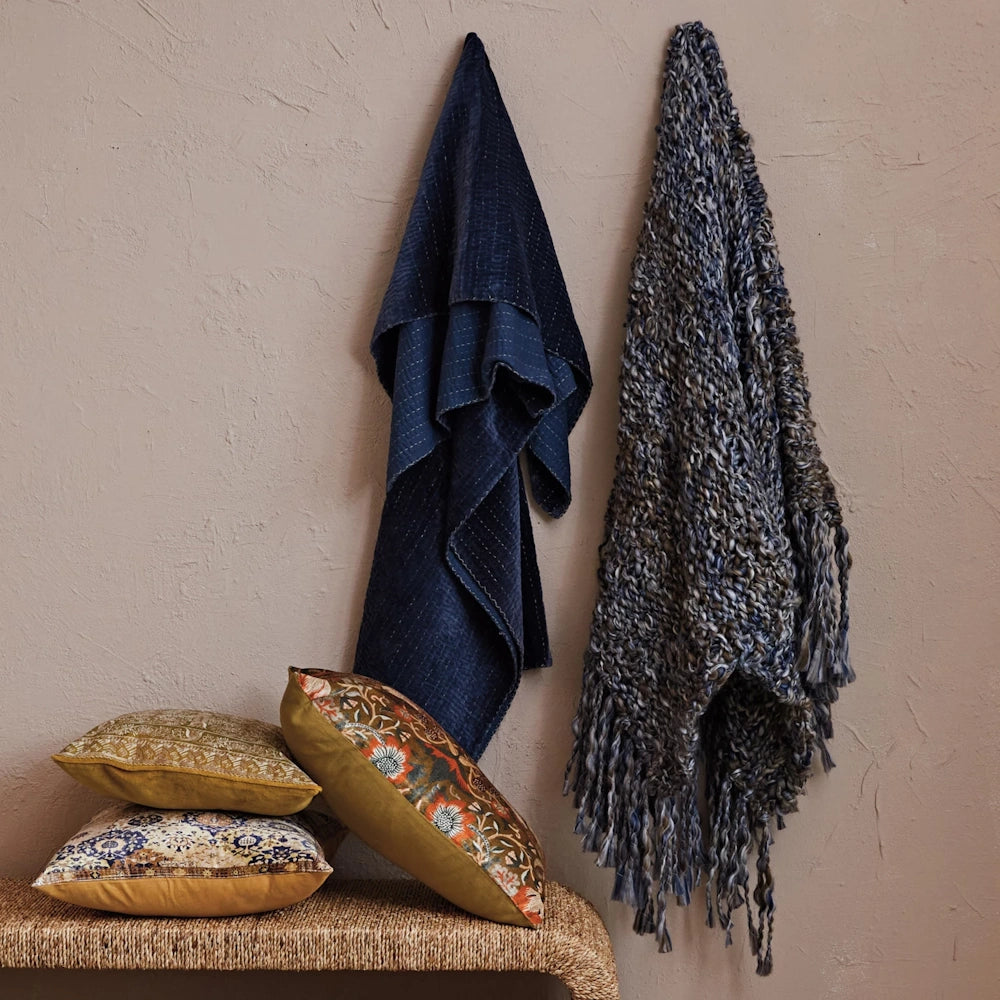 Bohemian home decor featuring pattern throw pillows on a wicker bench with hanging navy blue and chunky knit blankets.