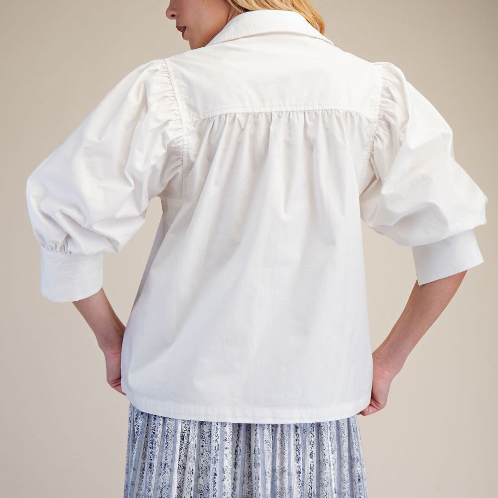 Back view of a white cotton poplin shirt featuring gathered details, puff sleeves, and a folded collar.