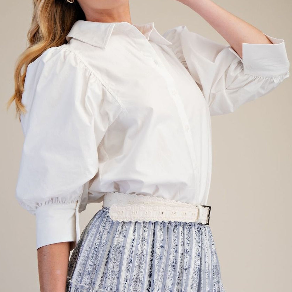 Side profile of a white poplin button-down shirt with voluminous puff sleeves tucked into a patterned skirt.