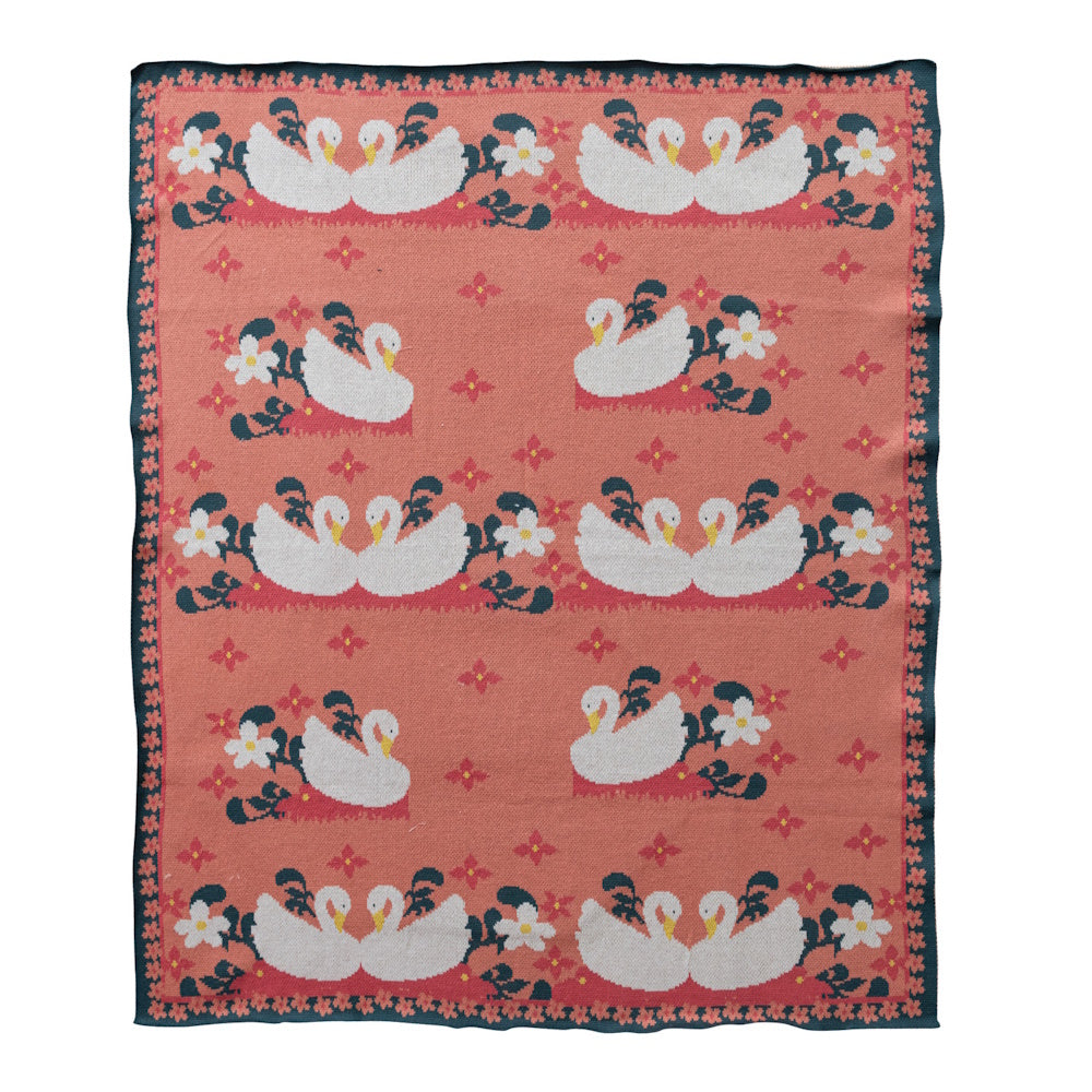 Pink cotton knit baby blanket featuring white swans and floral patterns with a decorative border.