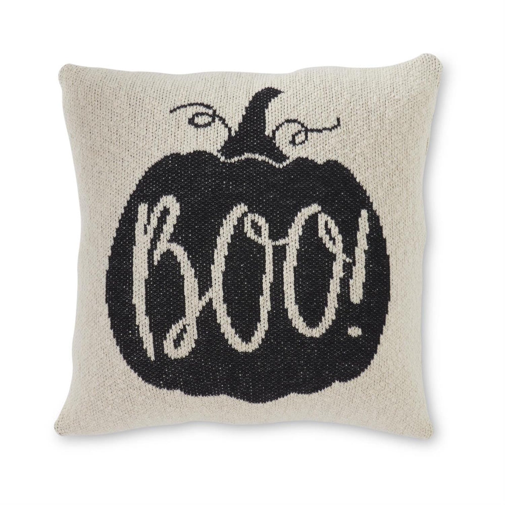 A square cream knit pillow featuring a black pumpkin silhouette with the word "BOO!" in white lettering.