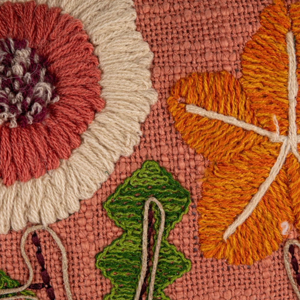 Close-up of embroidered floral pillow with textured orange leaf, pink flower, and green leaf on terracotta burlap fabric.