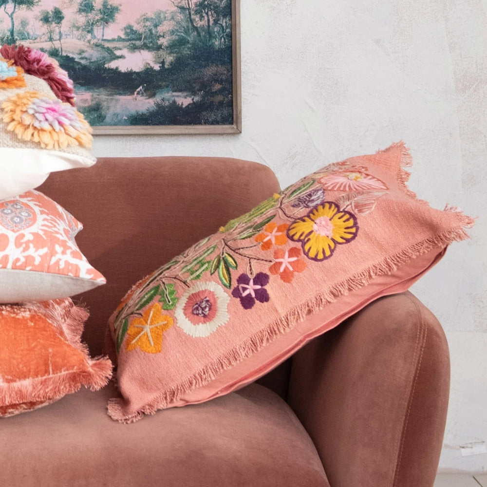 Embroidered floral lumbar pillow with fringe on a dusty rose velvet sofa with decorative cushions.