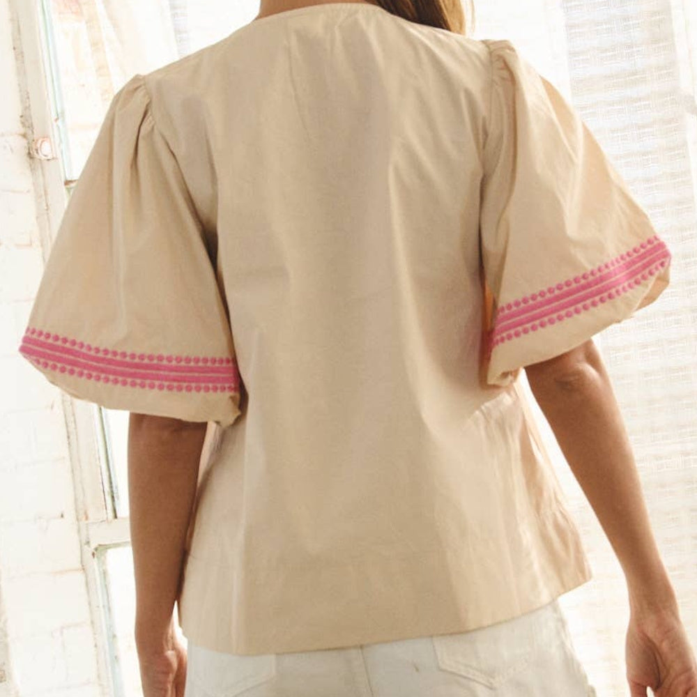 Back view of a beige cotton top featuring wide, flared sleeves with pink embroidered trim along the cuffs.