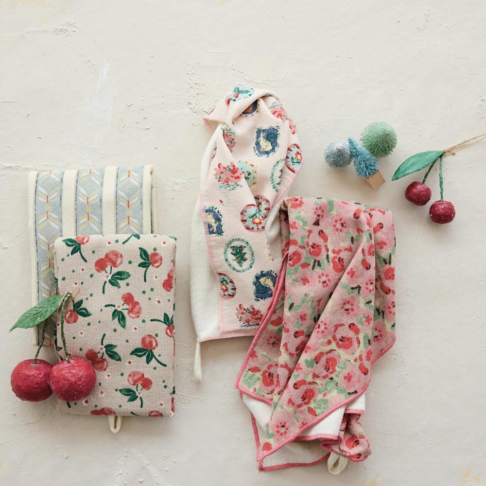 A set of four patterned cotton tea towels displayed with decorative cherries and small bottle brush trees.