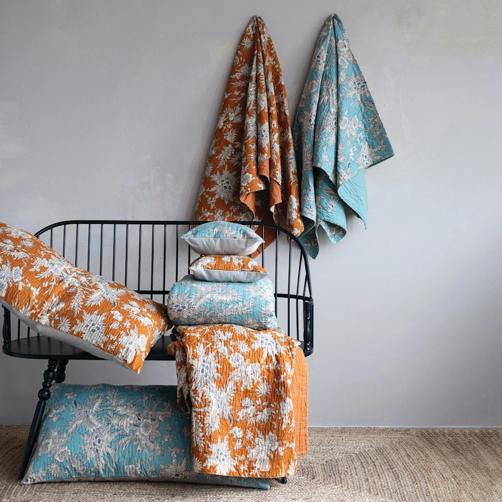 Floral cotton voile bed cover and shams in orange and teal draped over a black bench with floral patterns.