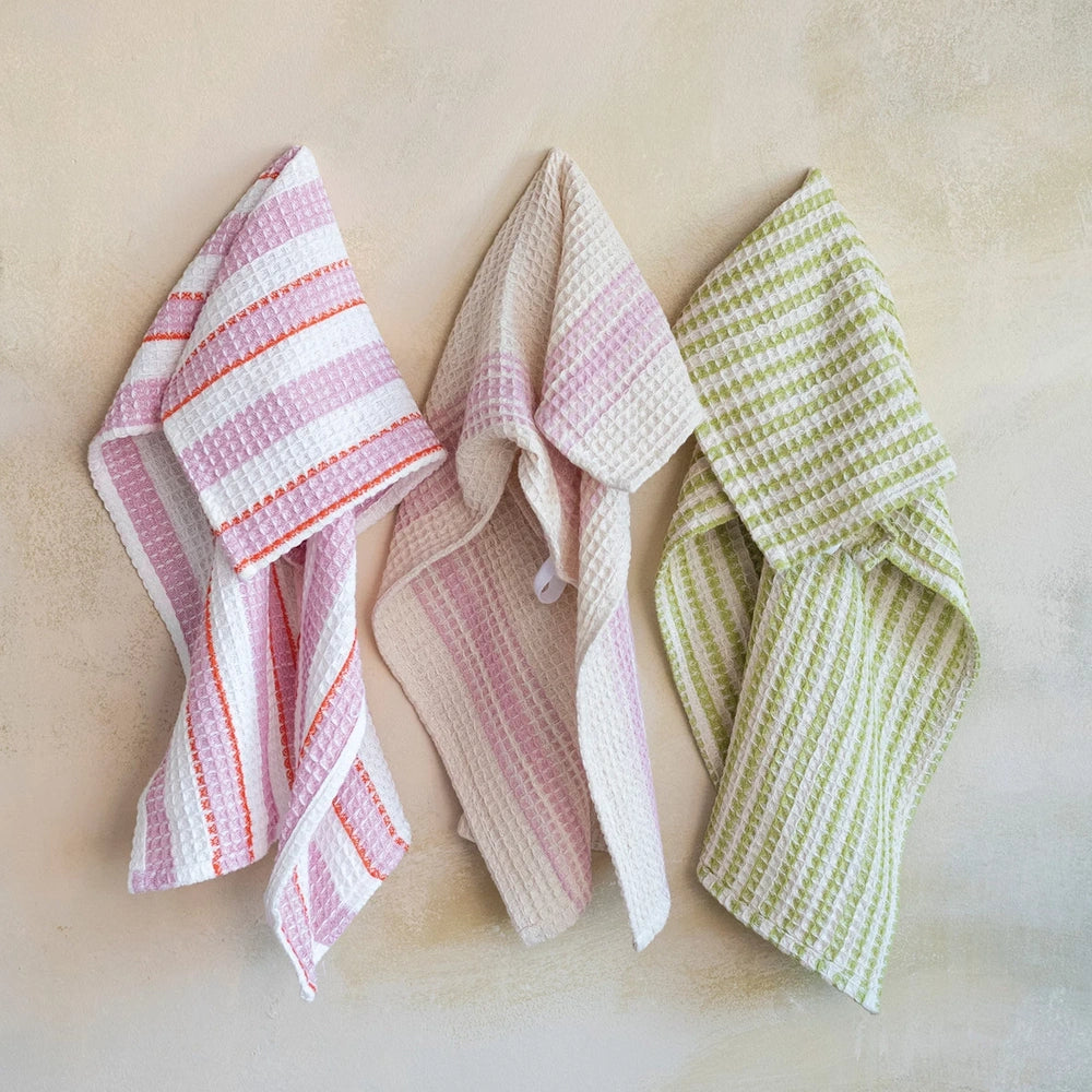 Cotton waffle weave tea towels with pink and green stripes. Absorbent, textured kitchen hand towels hanging on a wall.