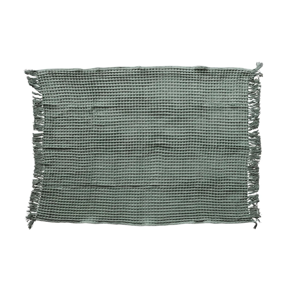 Sage green cotton waffle weave throw blanket with fringe trim.