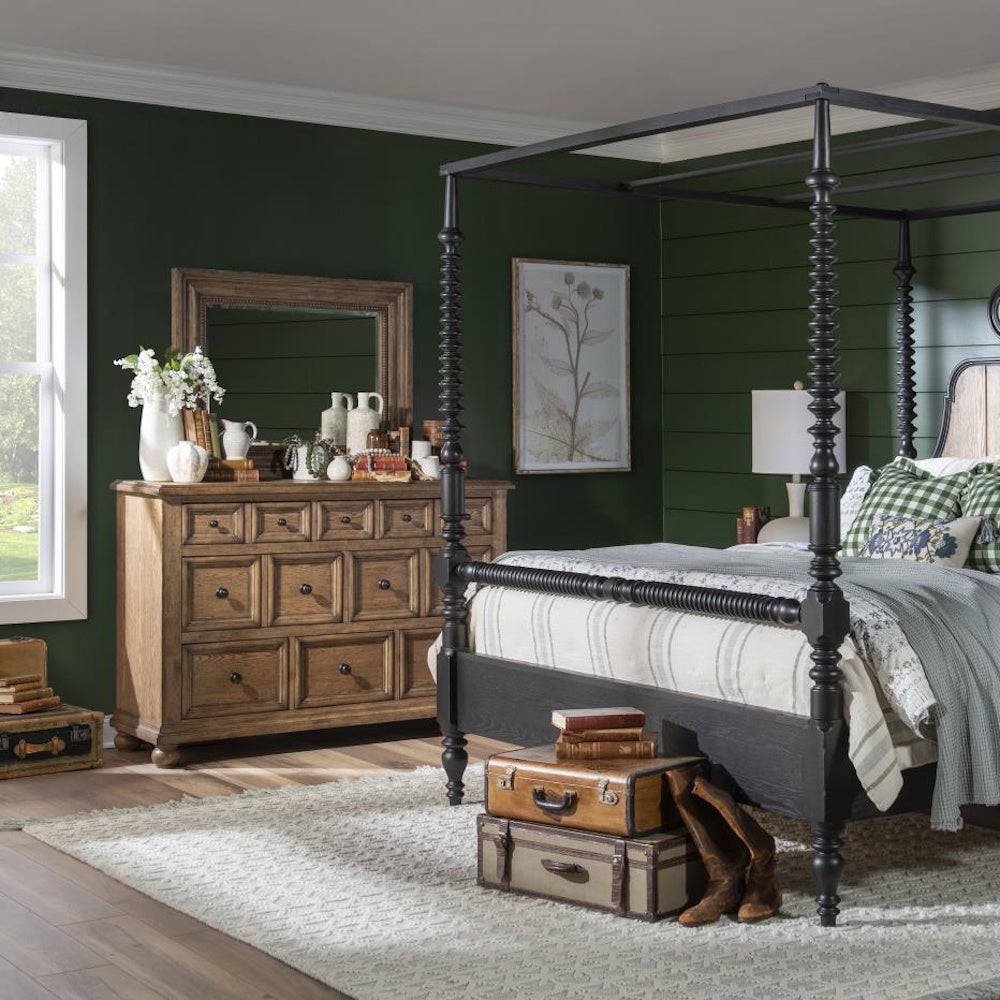 Rustic bedroom with a wood dresser and mirror beside a black canopy bed and vintage decor.