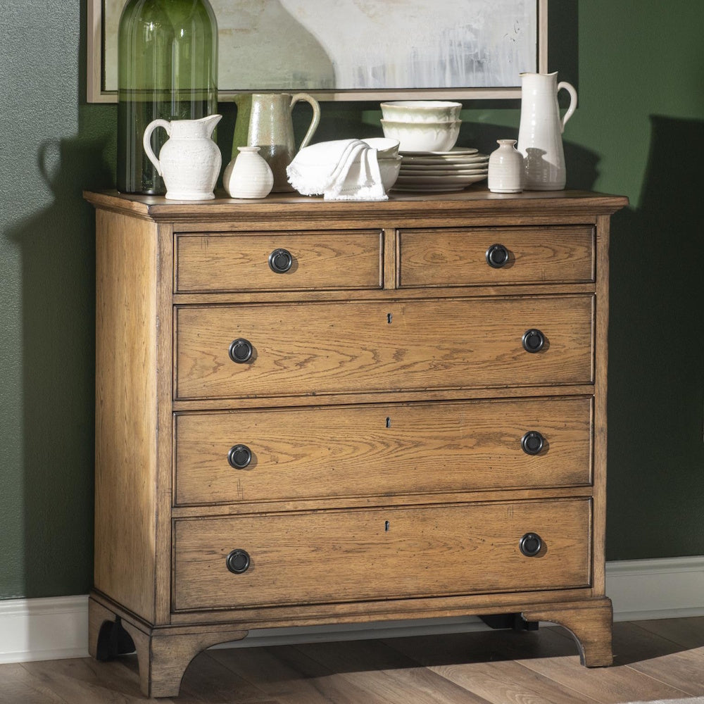 Rustic wood five drawer chest styled with ceramic pitchers, dishes and decor against a green wall.
