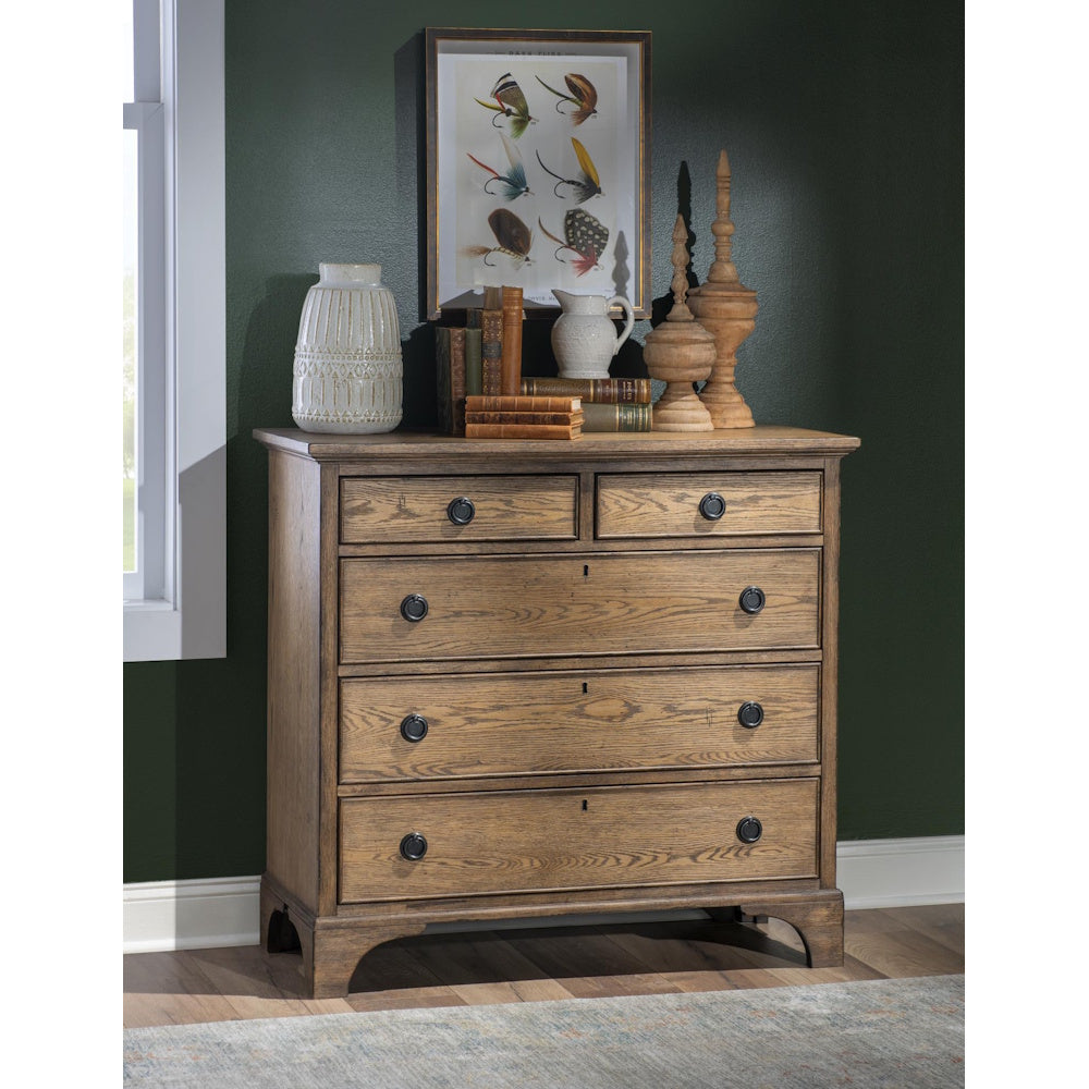 Rustic wood five drawer chest styled with books, vases and framed artwork against a dark green wall.