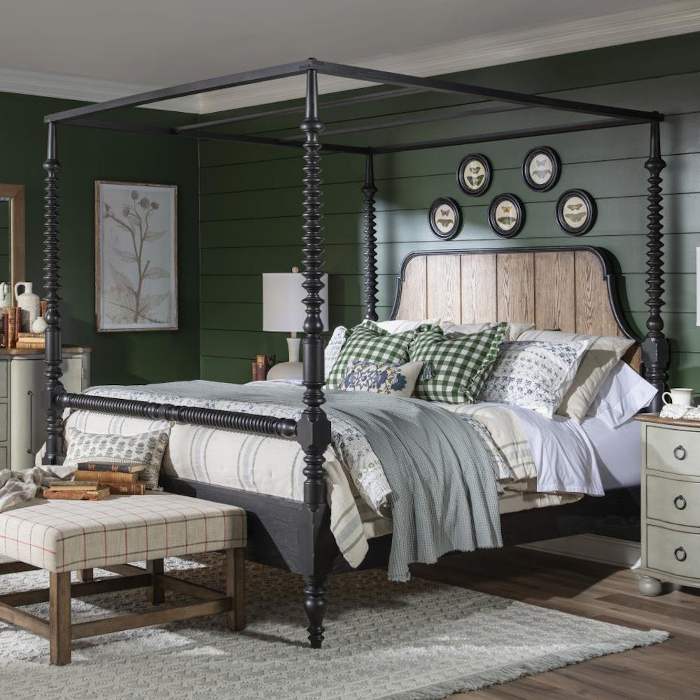 Black bobbin post canopy bed with a wood headboard, styled with layered bedding in a green bedroom.