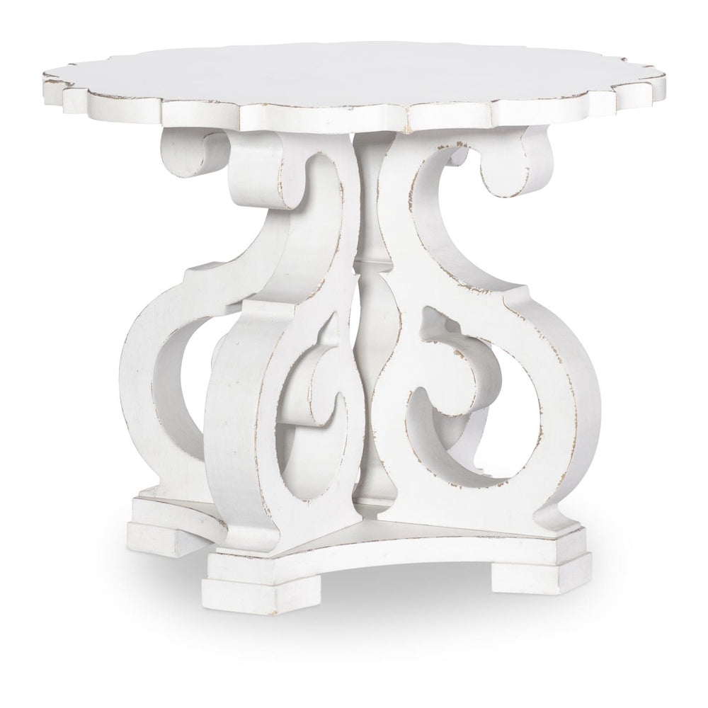 White distressed end table with ornate scrollwork pedestal base and scalloped tabletop on gray background.