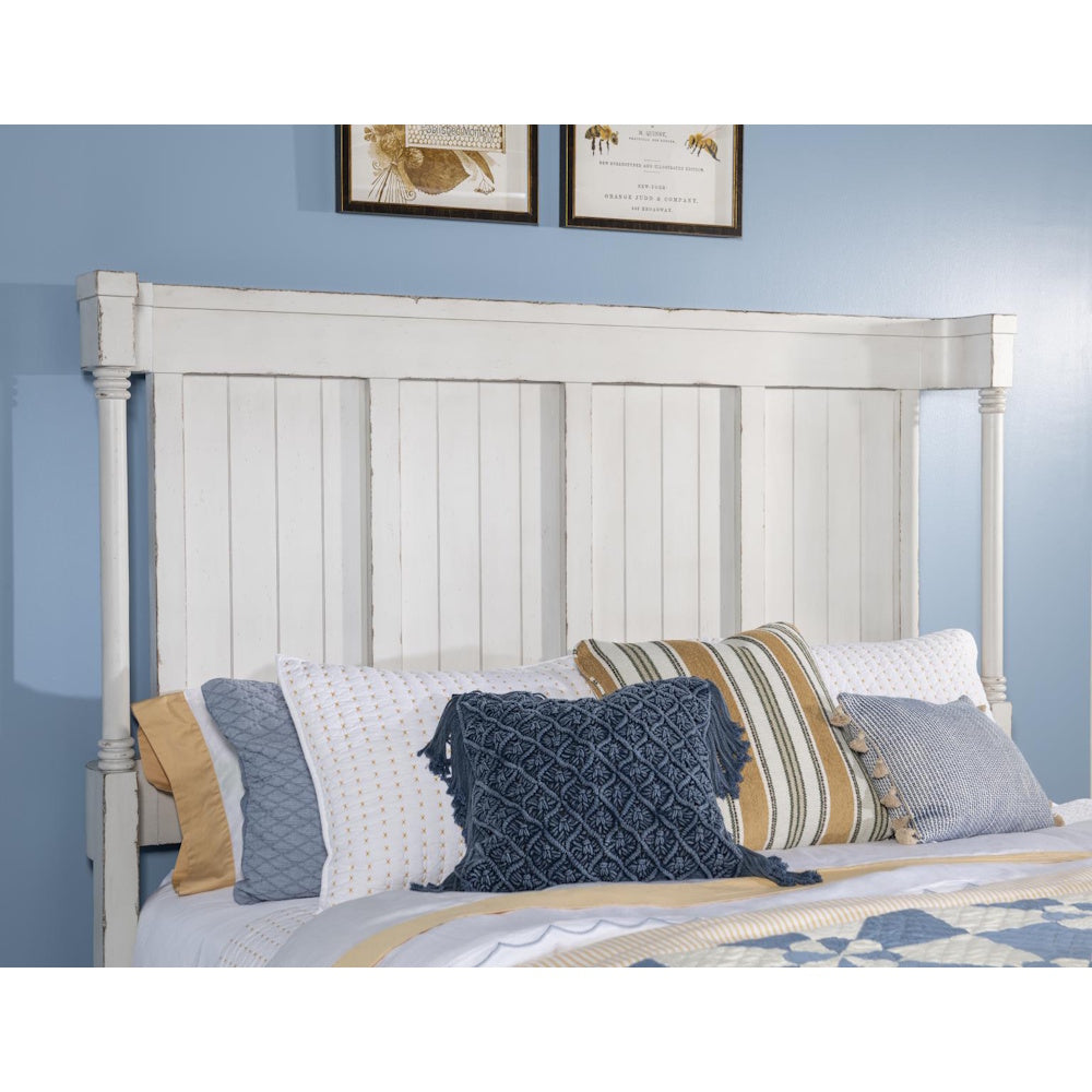 White rustic beadboard headboard with multiple decorative pillows on a bed against a blue wall.