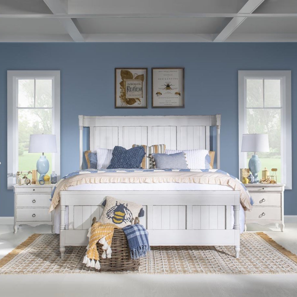 White wooden king bed in a blue bedroom with matching nightstands and a woven rug.