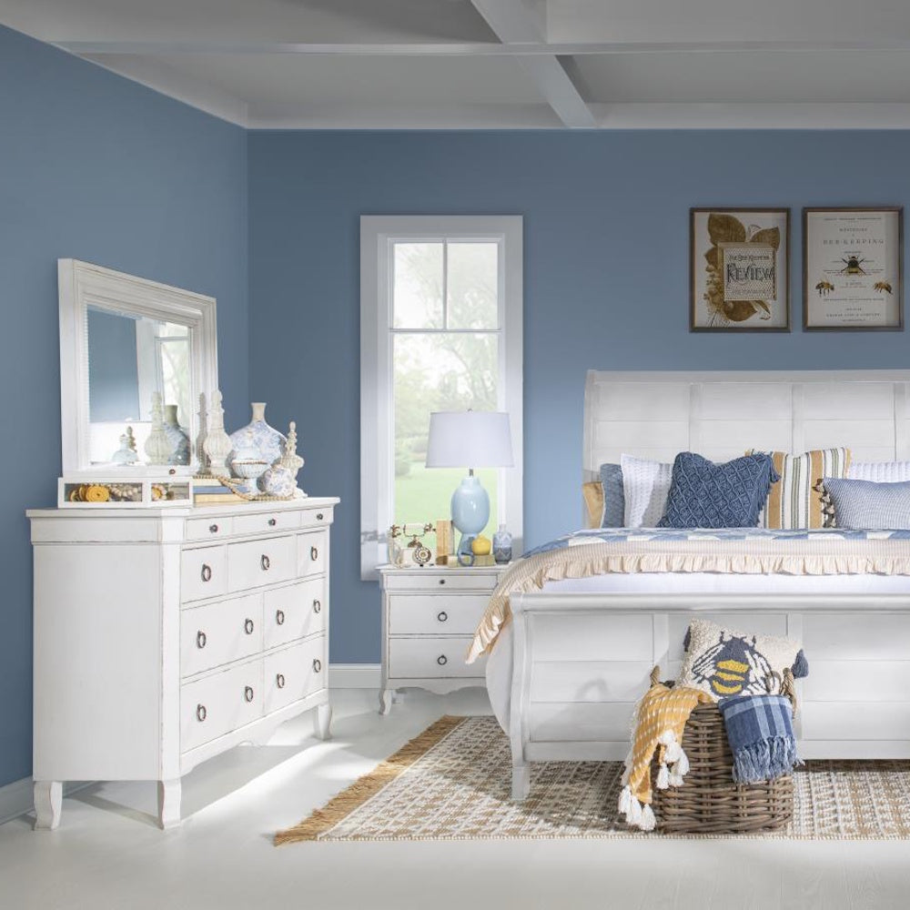 A bright blue bedroom featuring a white wooden bed, matching dresser with mirror, and a nightstand.