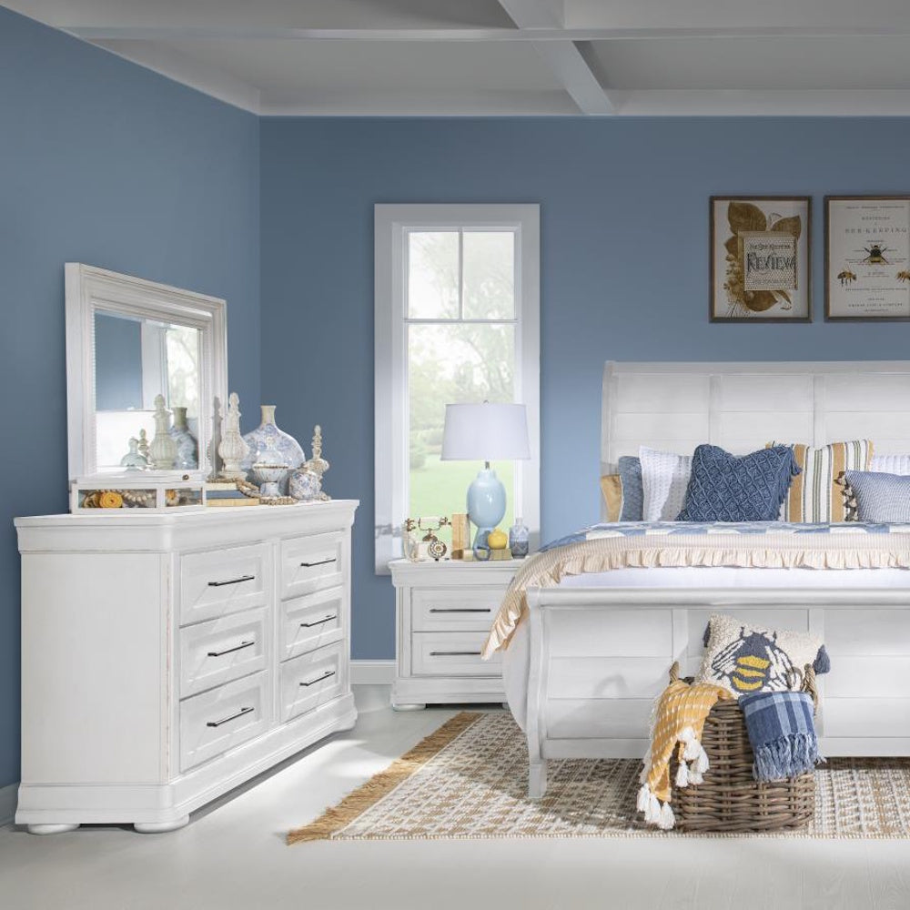 A white bedroom set with a dresser, mirror, and bed in a room with blue walls and country decor.