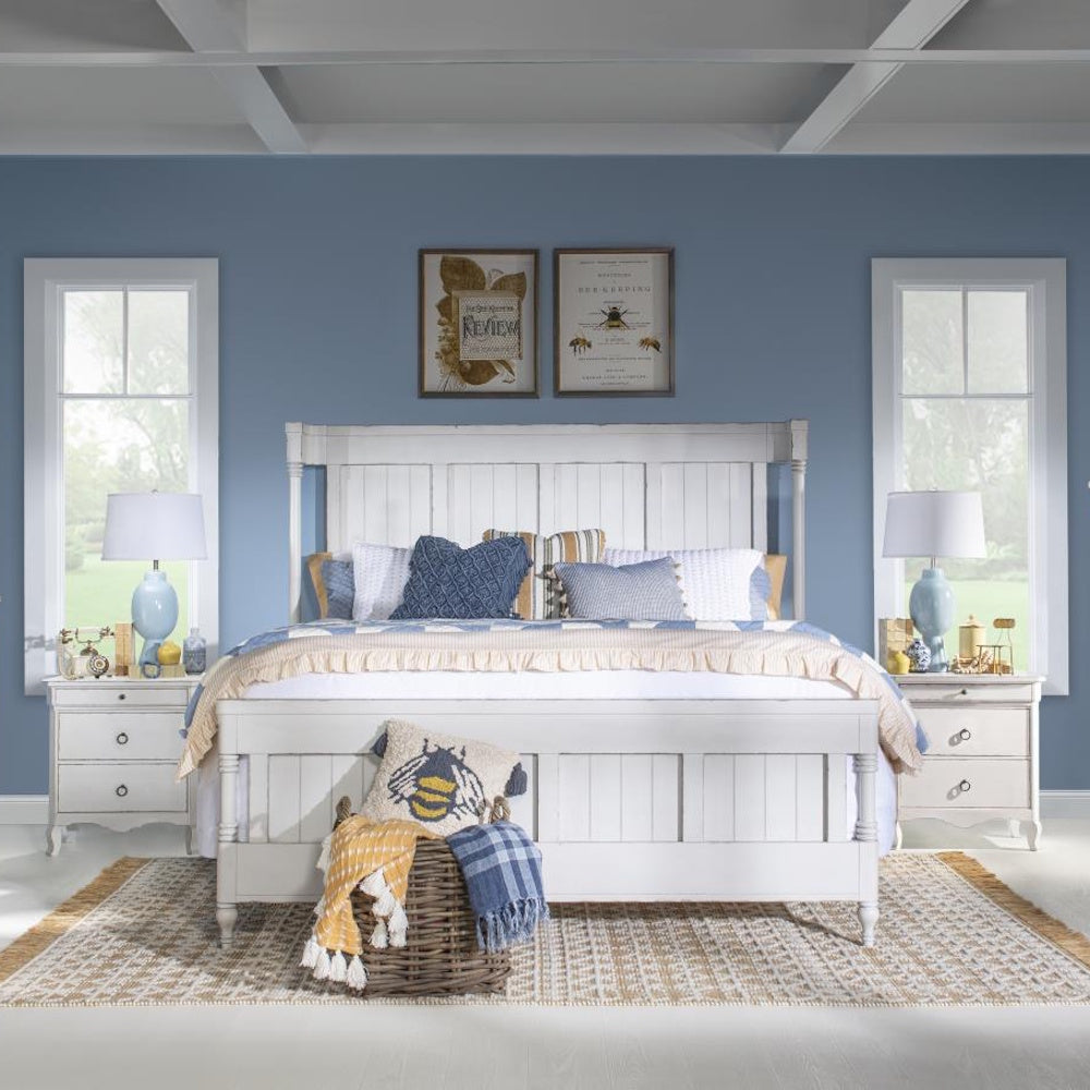 White paneled queen bed styled with blue and yellow bedding, matching nightstands, and ceramic lamps.