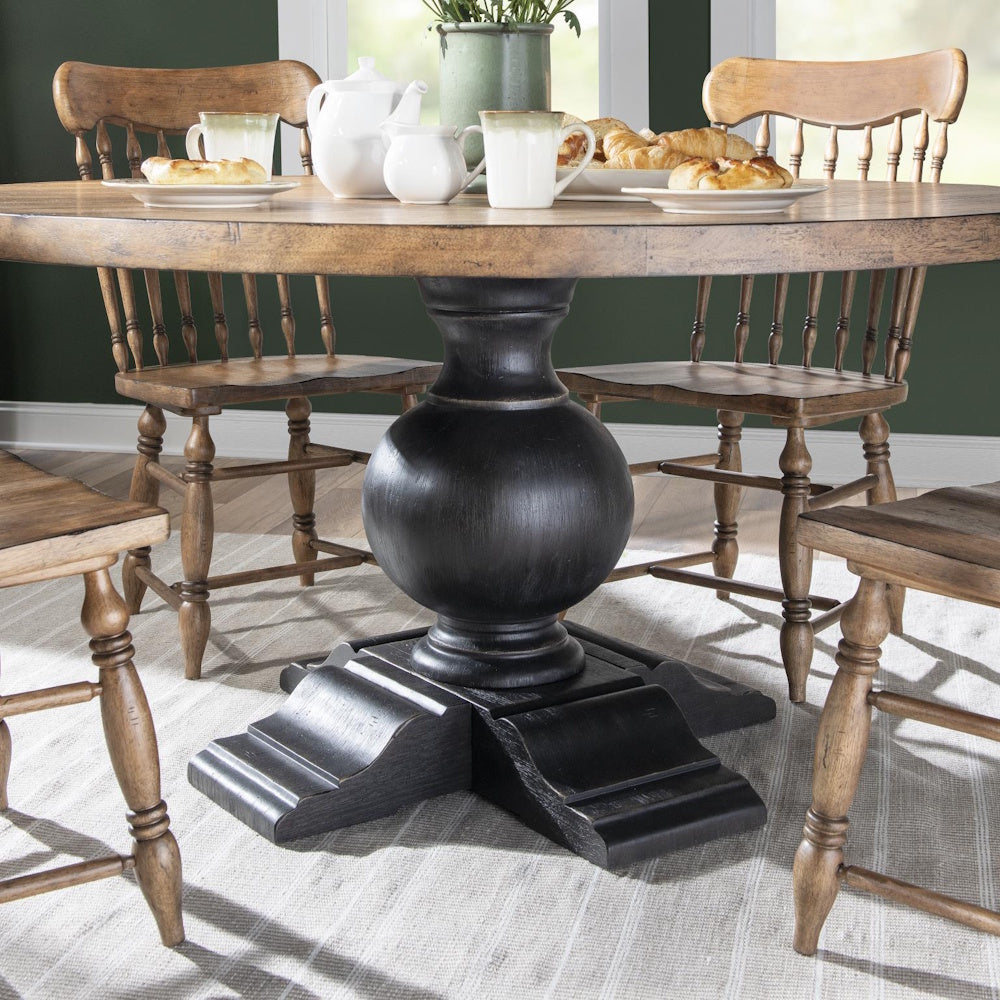 Round wooden dining table with a thick black pedestal base, surrounded by matching wooden chairs.