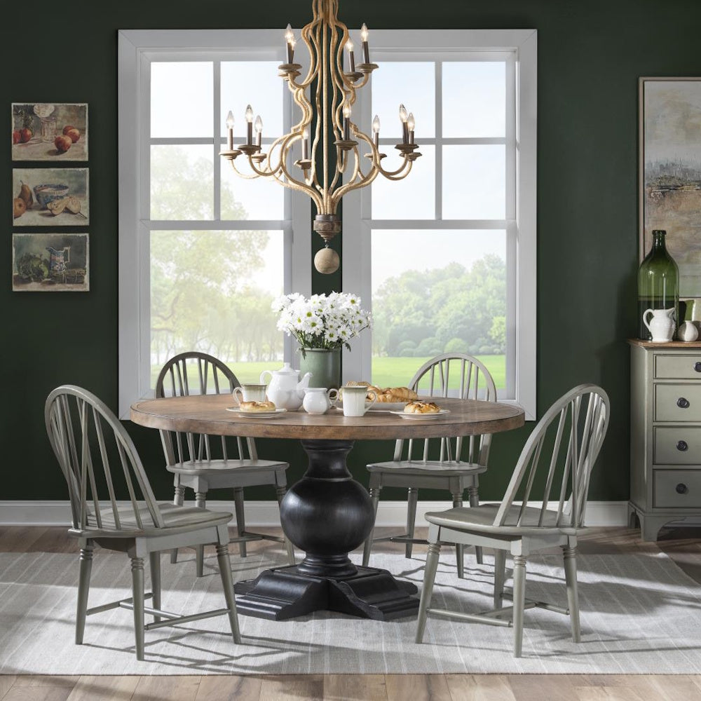 A round wooden dining table with a black pedestal base, surrounded by four grey chairs under a chandelier.