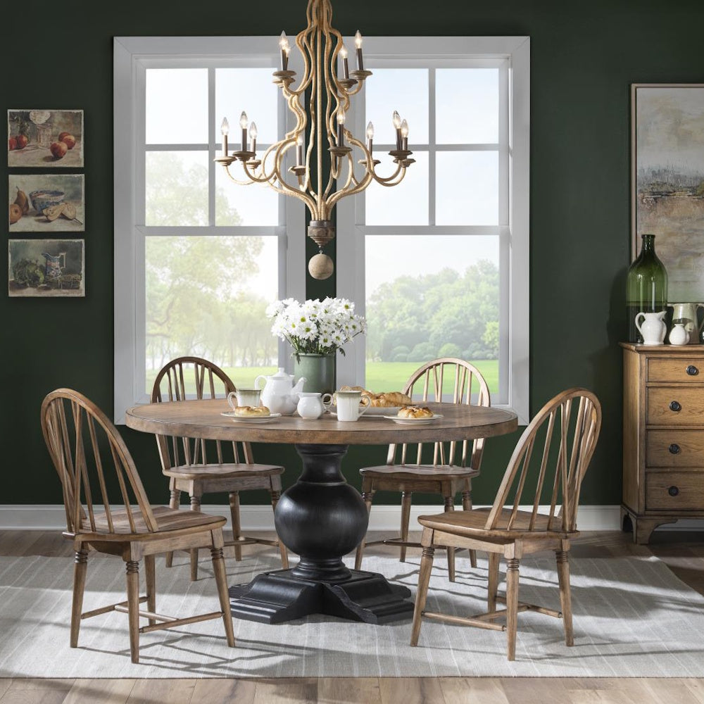 A round wooden dining table surrounded by four matching chairs under a large chandelier in a dining room.