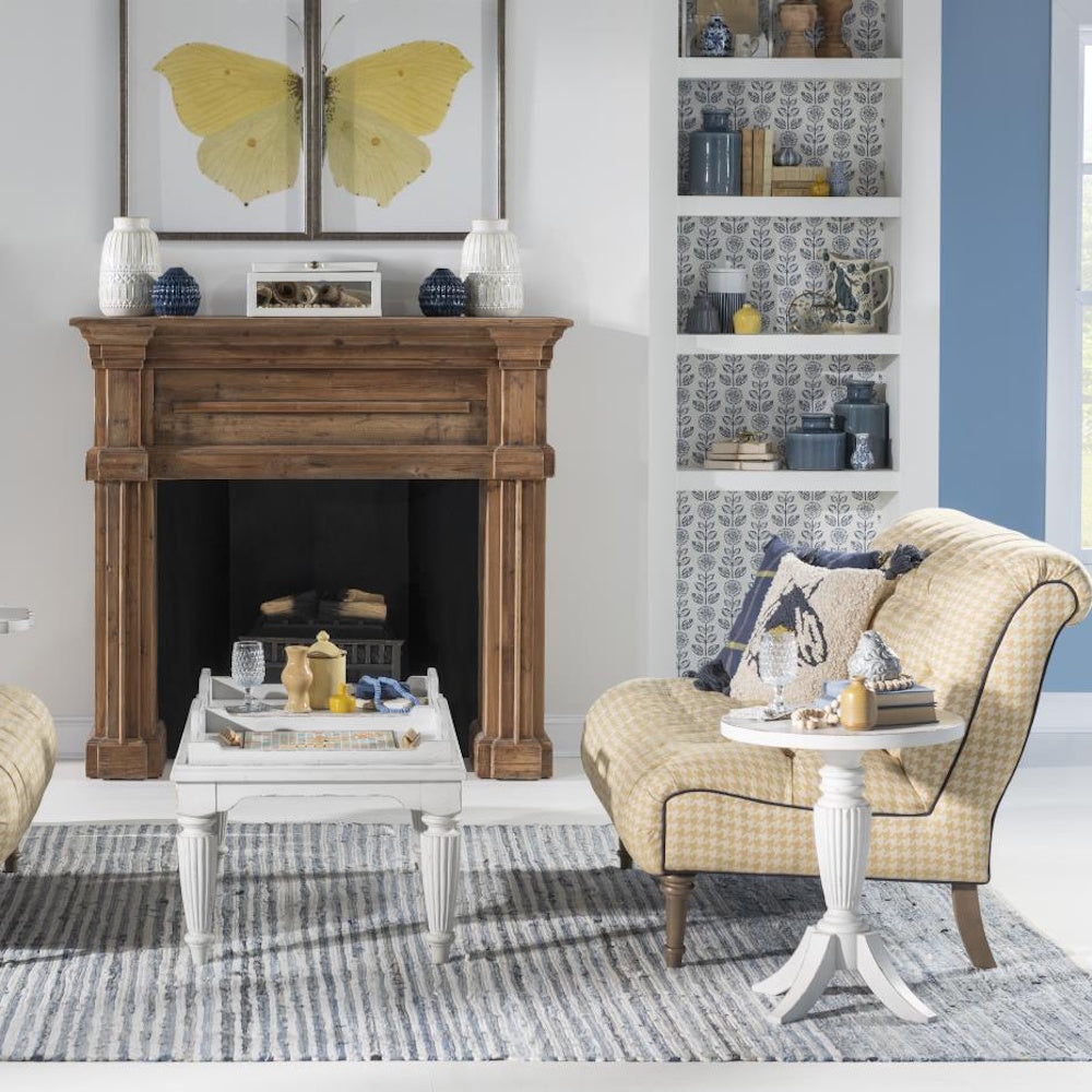 A cozy living room with a wooden fireplace mantel, a yellow armchair, and a small white round end table.