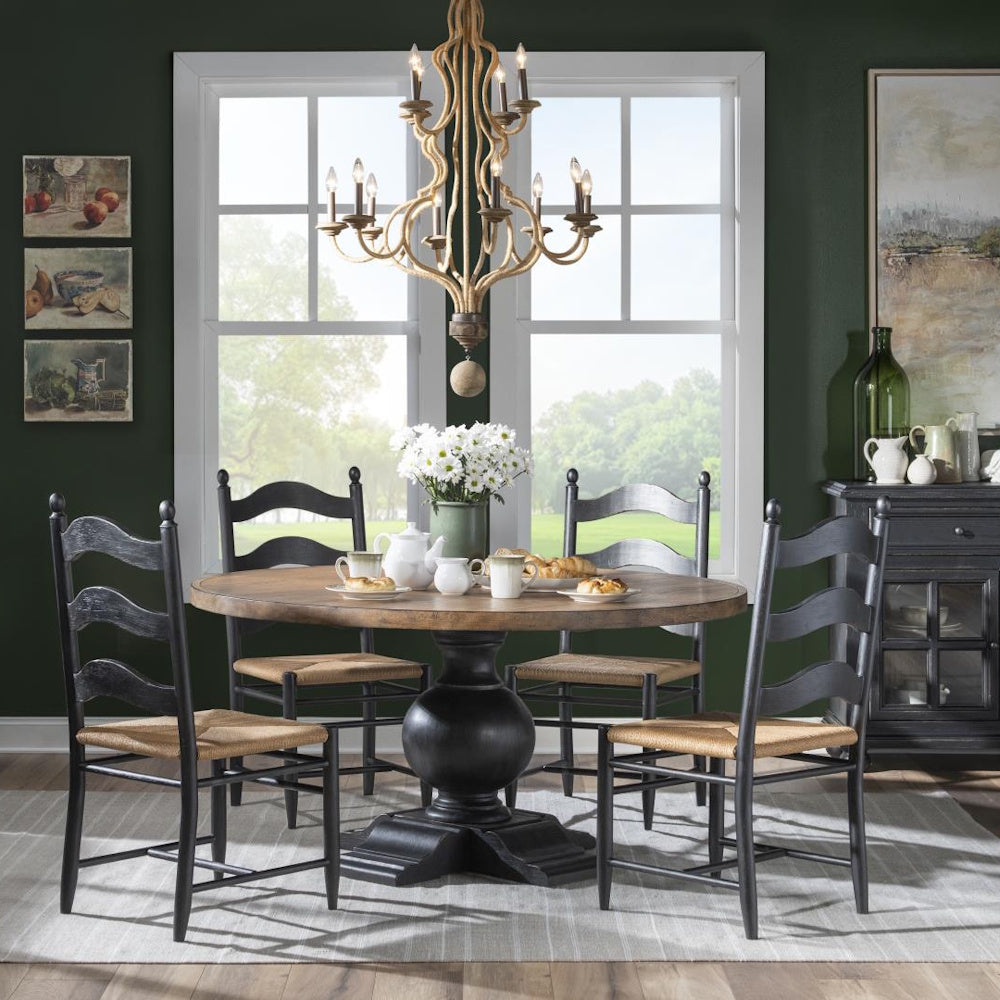 Dining room with round pedestal table, four gray ladder-back chairs, chandelier, and dark green walls.